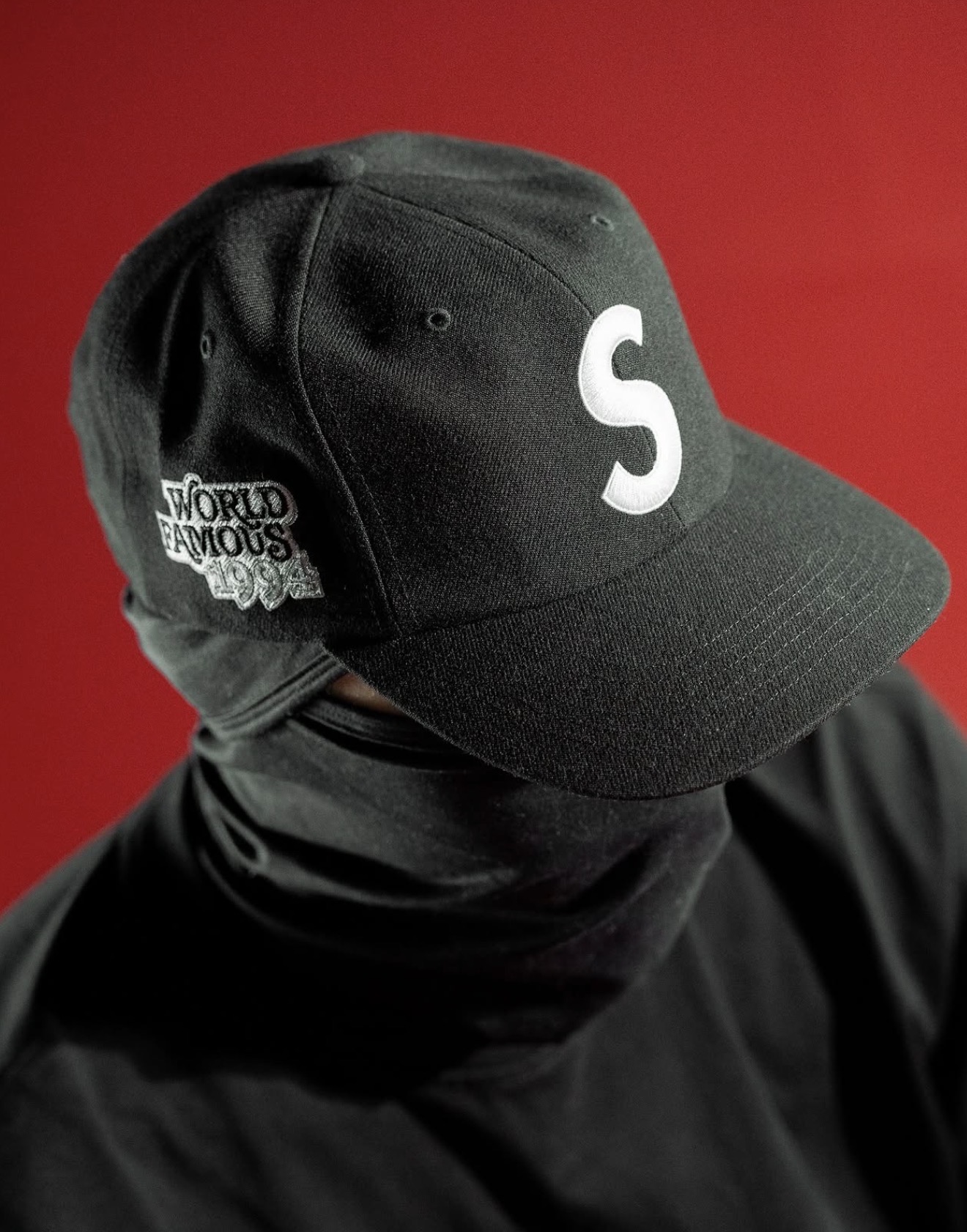 Black Supreme World Famous 1994 cap worn against a red backdrop — Holy Grail