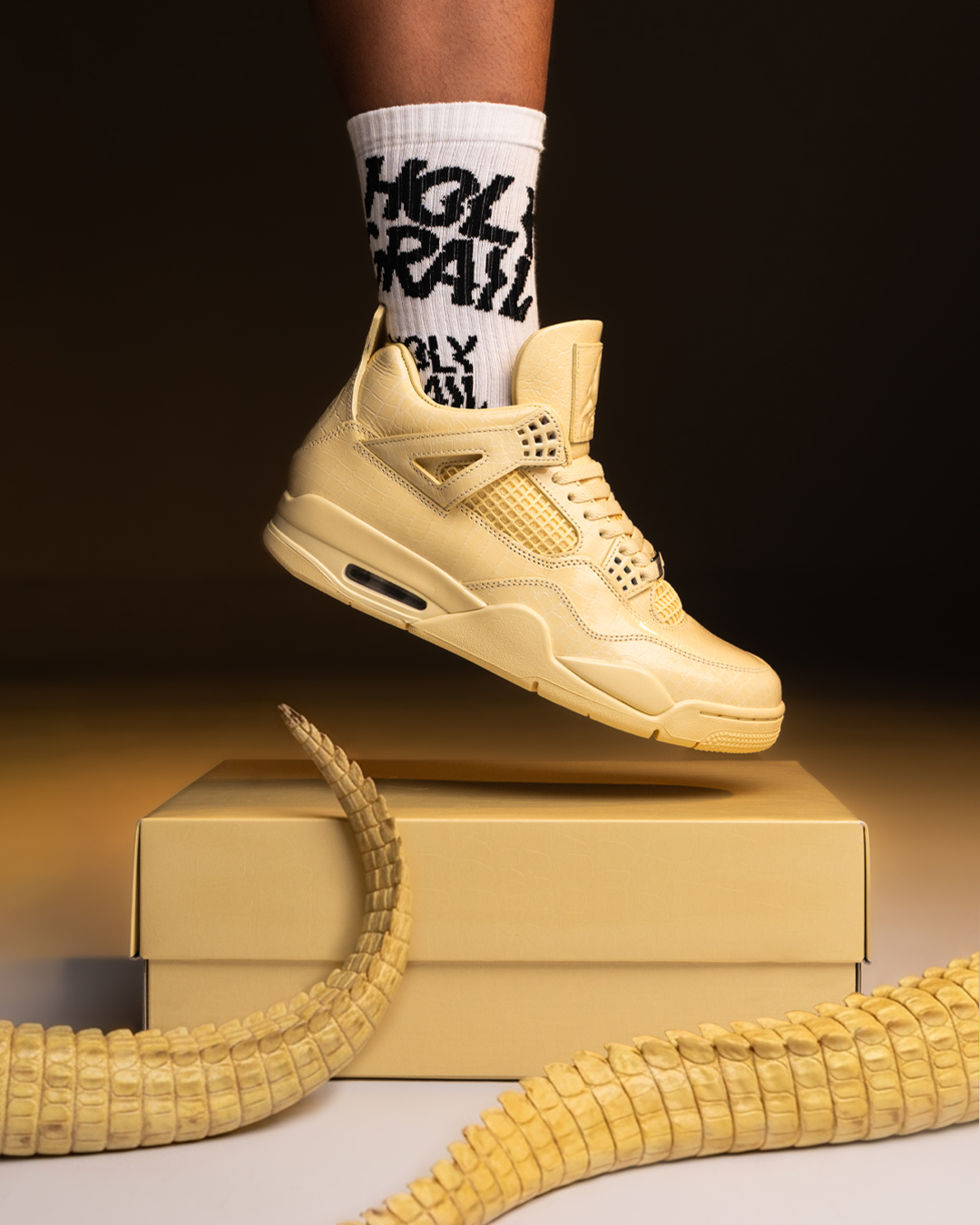 Jordan 4 amarillo con textura premium, medias Holy Grail y caja en fotografía editorial