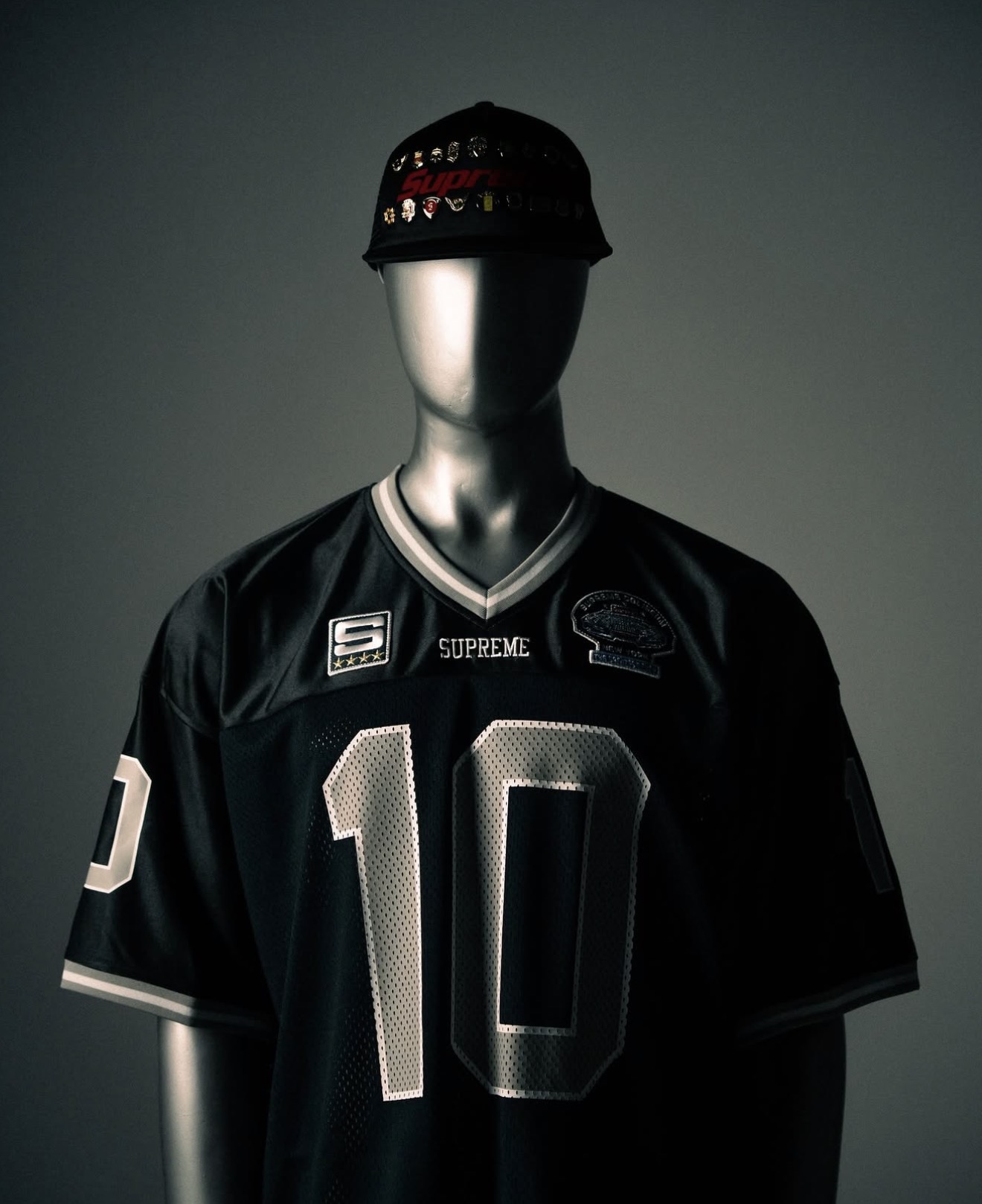 Black Supreme football jersey and pin-covered cap on a mannequin — Holy Grail