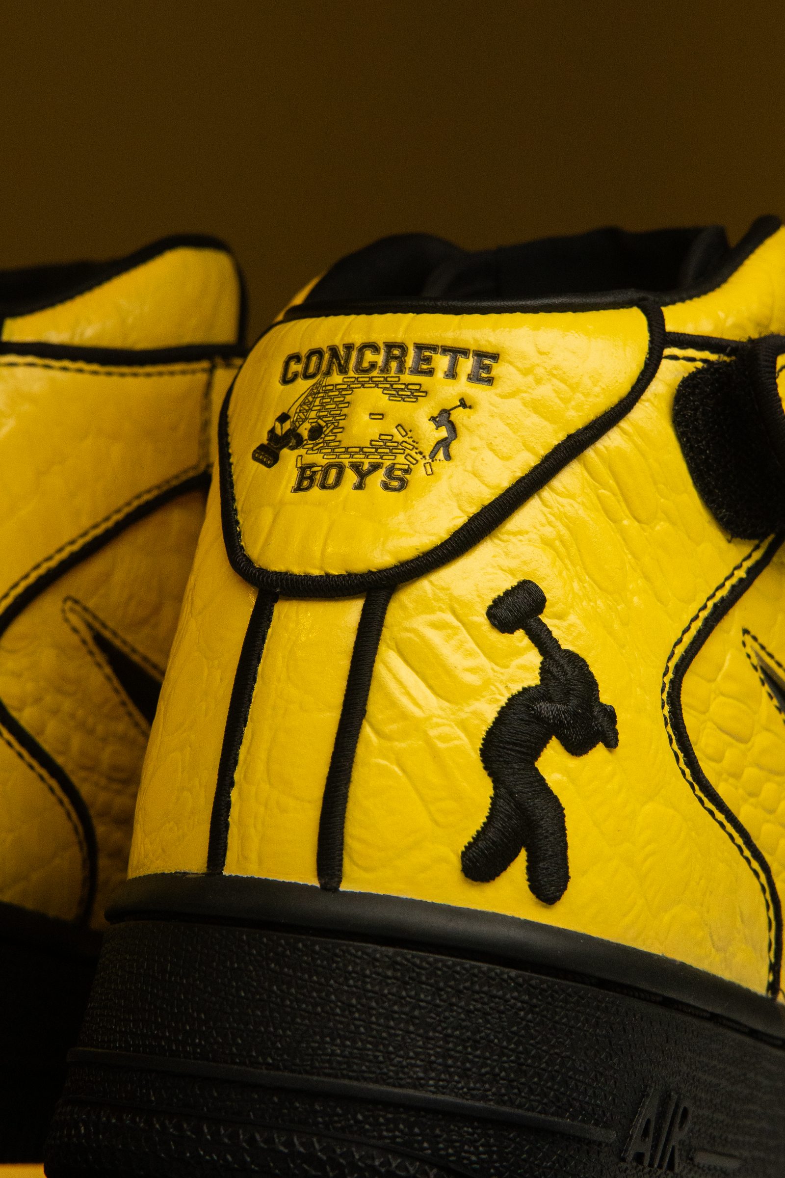 Primer plano del talón del Nike Air Force 1 Mid x Lil Yachty Opti Yellow con el logo Concrete Boys y bordados negros sobre cuero amarillo.